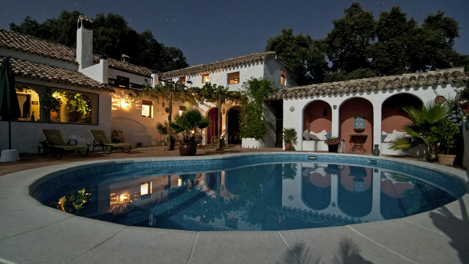 Whitewashed villa with arched verandas, warm lighting and a pool in the garden