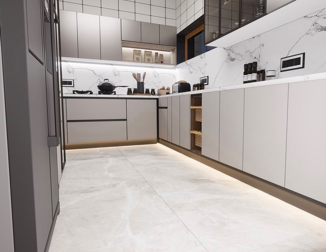 L-shaped modular kitchen with handleless ivory cabinets, a marble backsplash and plinth lighting